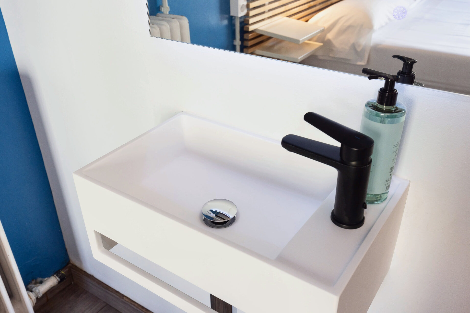 Lavabo blanc avec robinetterie noire et miroir éclairé.