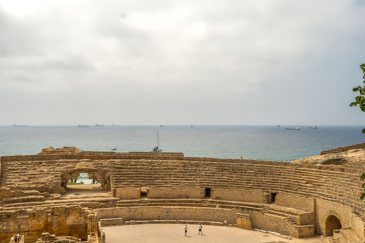 Gradins de l'amphithéâtre romain face à la mer, navires à l'horizon.
