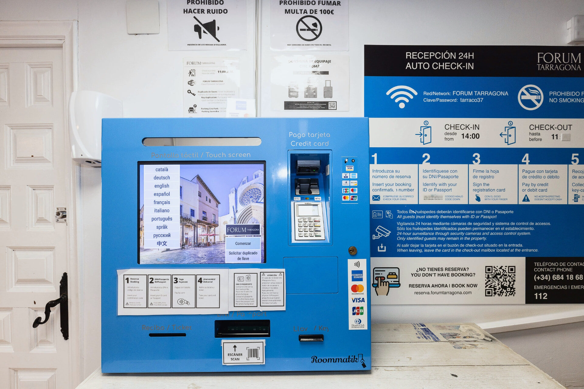 Màquina d'auto check-in amb pantalla tàctil i instruccions a la recepció de l'hostal.