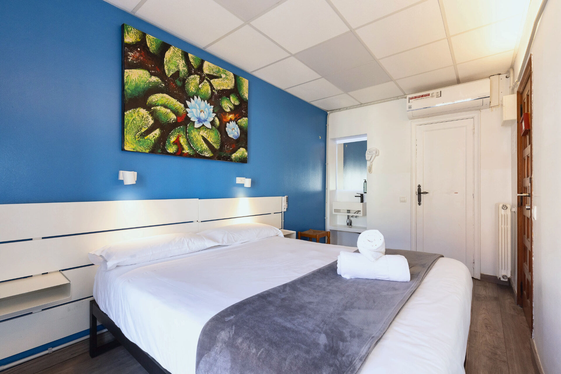 Chambre double avec mur bleu, lavabo et tableau de nénuphars.